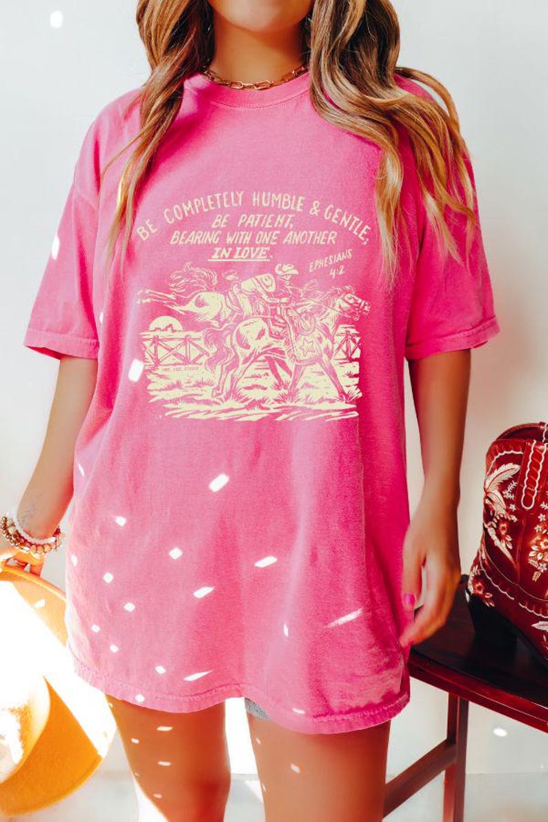 K&ouml;nnte beinhalten: Rosafarbenes Oversize-T-Shirt mit einer Vintage-Grafik von Pferden und einem Zitat: "Seid vollkommen dem&uuml;tig und sanftm&uuml;tig. Seid geduldig und ertragt einander in Liebe. Epheser 4,2".