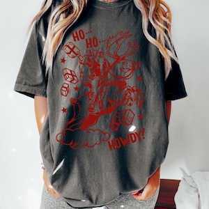 May include: A dark gray t-shirt with a red graphic of a person riding a reindeer with the words "Ho Ho... Howdy!" printed on it.