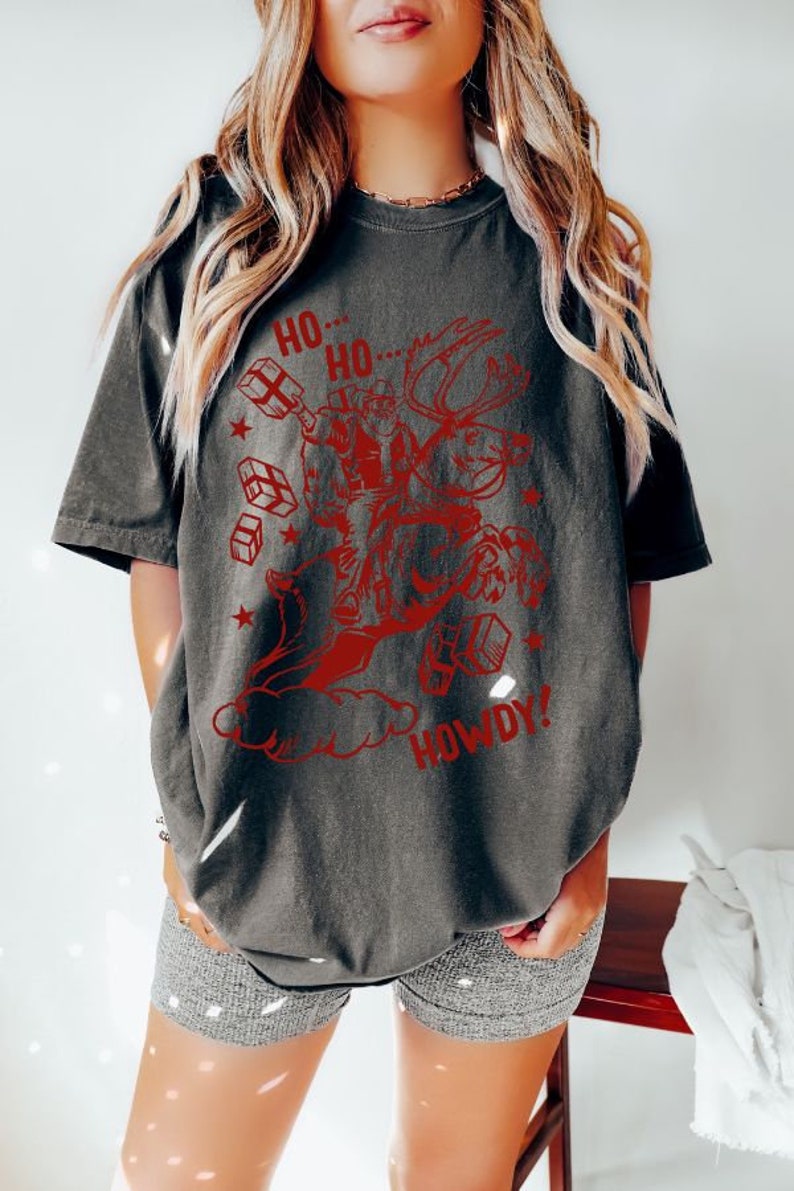 May include: A dark gray t-shirt with a red graphic of a person riding a reindeer with the words "Ho Ho... Howdy!" printed on it.
