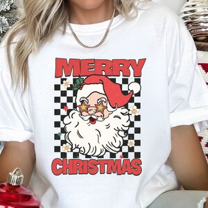 K&ouml;nnte beinhalten: Wei&szlig;es T-Shirt mit einem rot-schwarzen Karomuster, einem Cartoon-Weihnachtsmann mit Sonnenbrille und dem Text "Frohe Weihnachten".