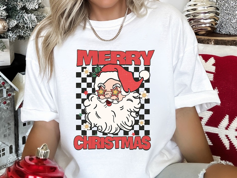 K&ouml;nnte beinhalten: Wei&szlig;es T-Shirt mit einem rot-schwarzen Karomuster, einem Cartoon-Weihnachtsmann mit Sonnenbrille und dem Text "Frohe Weihnachten".