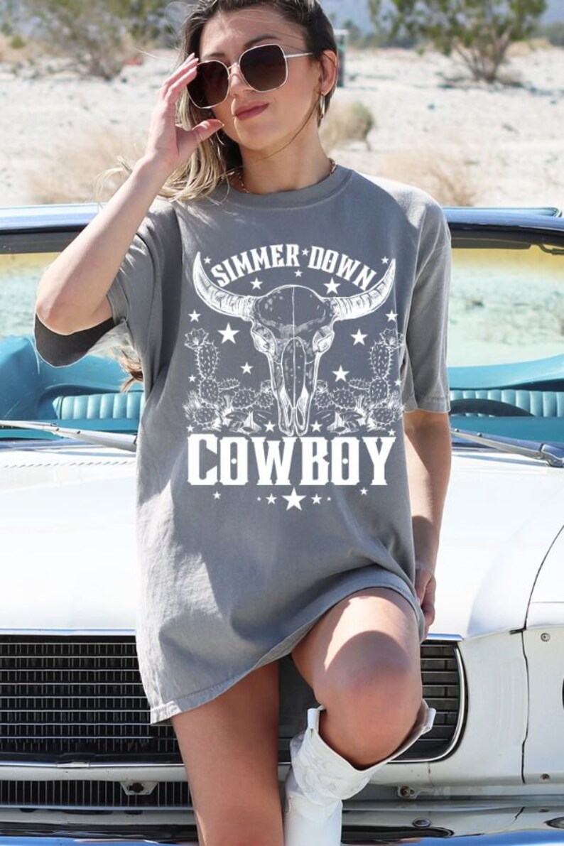 May include: A gray oversized t-shirt with a white graphic of a bull skull with horns, cactus, and stars. The text "SIMMER DOWN COWBOY" is printed on the shirt.