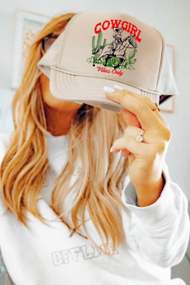 May include: A beige trucker hat with a cowgirl riding a horse graphic and the text "Cowgirl Vibes Only".
