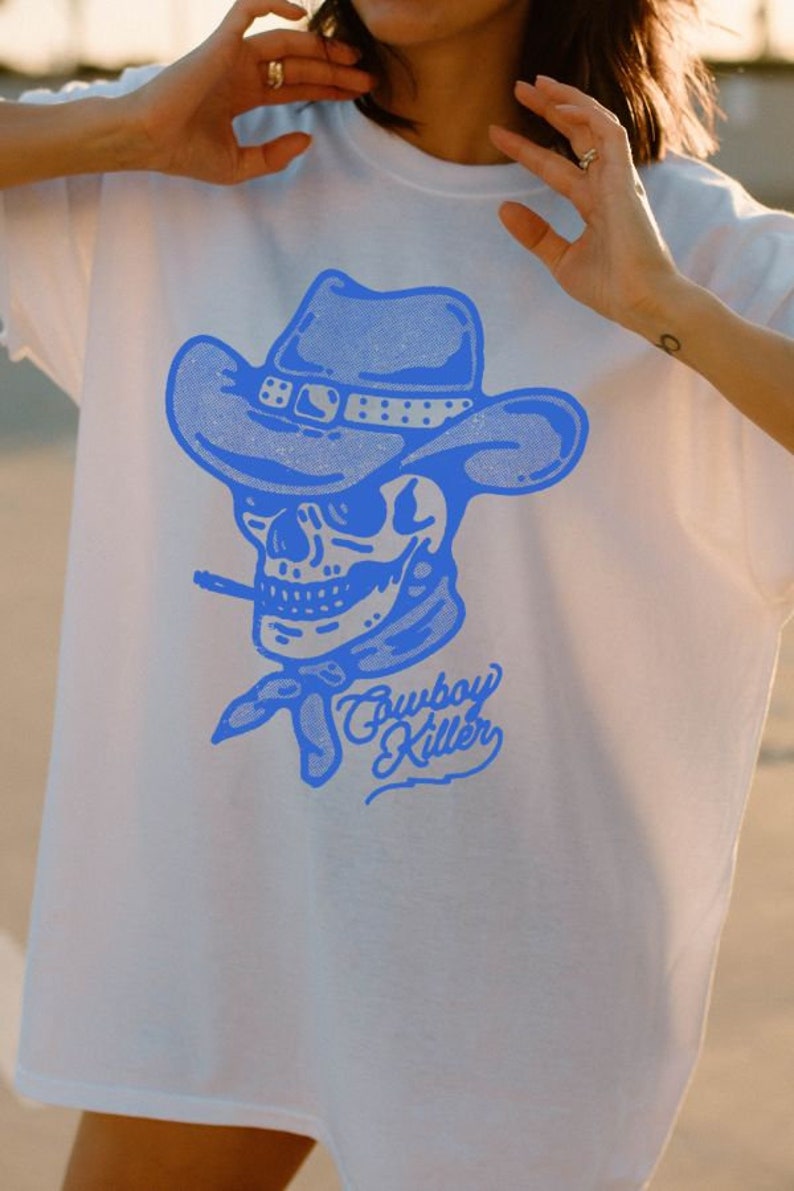 May include: A white t-shirt featuring a blue graphic of a skull wearing a cowboy hat and the text "Cowboy Killer".