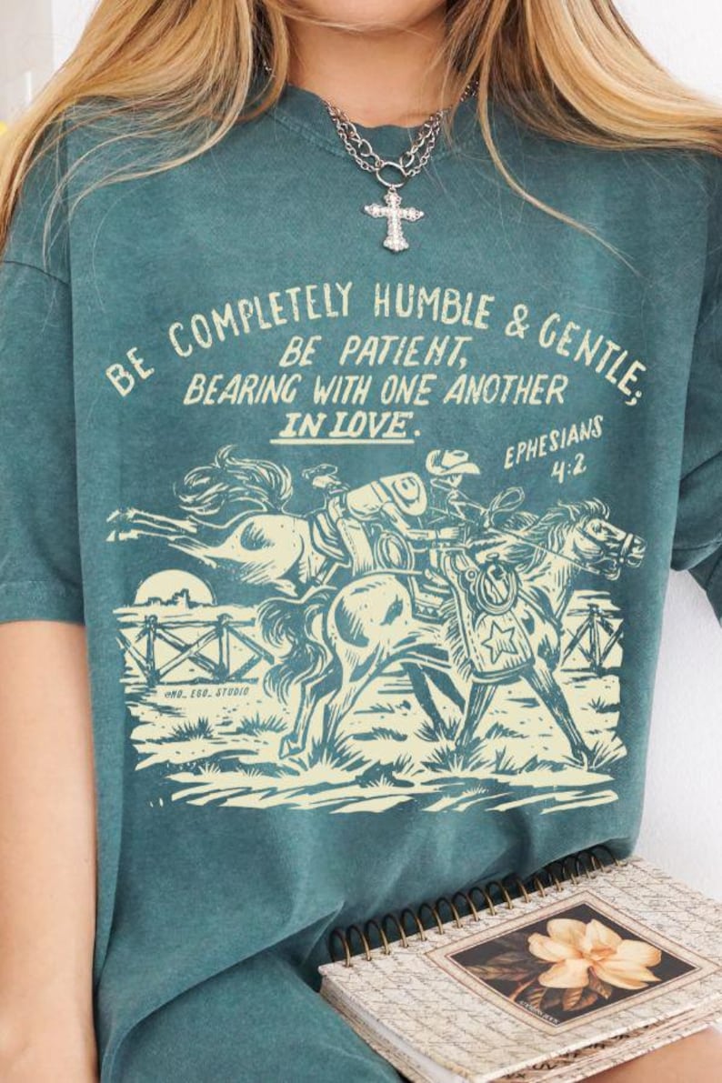 K&ouml;nnte beinhalten: Tealblaues T-Shirt mit einer Grafik im Vintage-Stil von zwei Pferden und einem Reiter. Der Text auf dem Shirt lautet "Be completely humble & gentle: Be patient, bearing with one another in love. Ephesians 4:2"