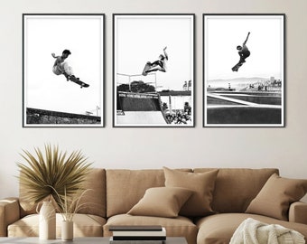 May include: Three black and white photographs of skateboarders performing tricks. The photos are framed in black frames and are hung on a white wall above a brown couch.