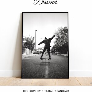 May include: Black and white photograph of a person skateboarding down a street. The person is wearing a jacket and has their arms outstretched. There are other people in the background.