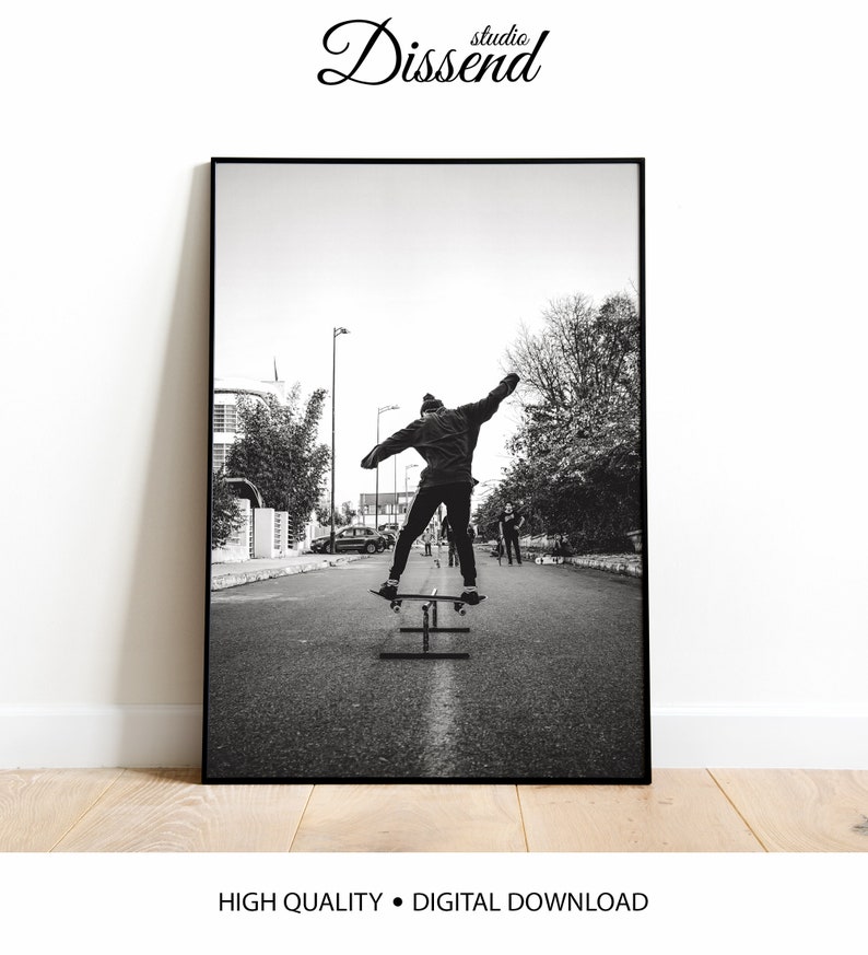 May include: Black and white photograph of a person skateboarding down a street. The person is wearing a jacket and has their arms outstretched. There are other people in the background.