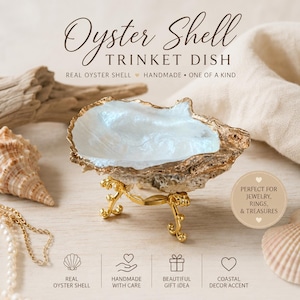 May include: A real oyster shell trinket dish with a pearlescent white interior and a textured, natural exterior. The shell is supported by a decorative gold-toned metal stand with ornate, curved legs. Text on the image reads Oyster Shell TRINKET DISH.