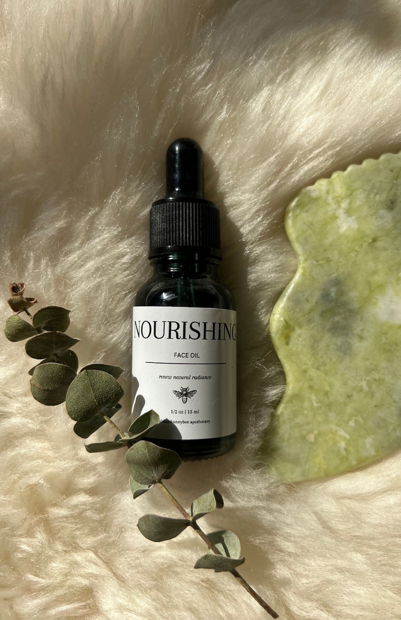 Homemade face oil great for use with gua sha tool. Image depicts the product set on a white background with a strand of eucalyptus and a jade gua shaw tool.