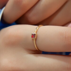 May include: A gold ring with a small, square, red gemstone.