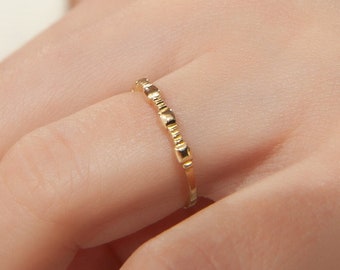 May include: A delicate gold ring with a series of small, square-shaped accents. The ring is worn on a hand with manicured nails, suggesting a focus on jewelry and accessories. The ring's design is simple yet elegant, suitable for everyday wear.