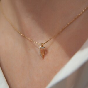 Puede incluir: Un collar de cadena de oro con un peque&ntilde;o colgante en forma de flecha puntiaguda adornado con diamantes.