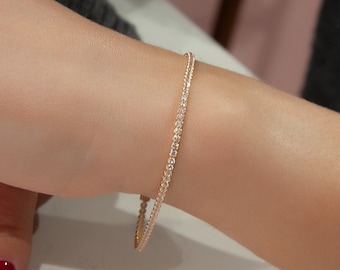 May include: A delicate gold bracelet with a row of small, clear stones. The bracelet is on a person's wrist.