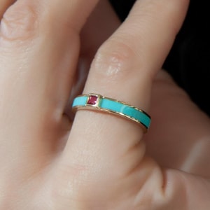 May include: A gold ring with a turquoise band and a small red gemstone.
