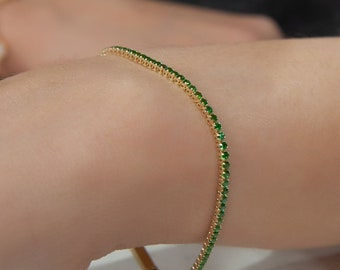 May include: A gold bracelet with a thin band of small green gemstones.