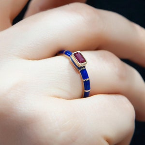 May include: A gold ring with a blue enamel band and a red rectangular gemstone.