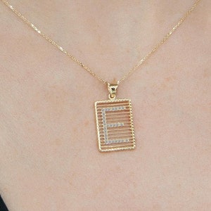 Puede incluir: Un collar de cadena de oro con un colgante con la letra 'E' rodeada de pequeños diamantes. El colgante es de forma rectangular.