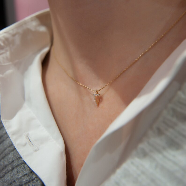 Puede incluir: Un collar de cadena de oro con un peque&ntilde;o colgante en forma de flecha puntiaguda adornado con diamantes.