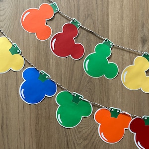 Pode incluir: Uma guirlanda colorida com tema Mickey Mouse com cabeças de Mickey Mouse vermelhas, laranja, amarelas, verdes e azuis enfiadas em um barbante branco e preto.