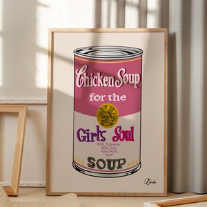 Op de afbeelding: Een roze en witte blikje kippensoep met de tekst "Chicken Soup for the Girls Soul" en "REAL Stories by REAL Girls About REAL Stuff SOUP". Het blikje heeft een gouden ster bovenaan en onderaan en een gouden zegel aan de zijkant. De tekst "Bóefin" staat in zwart rechtsonder.