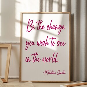 May include: A framed print with a white background and a pink inspirational quote that reads "Be the change you wish to see in the world." The quote is attributed to Mahatma Gandhi.