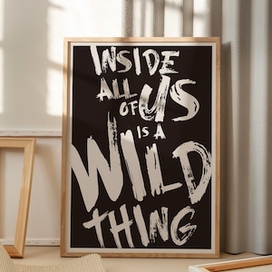 Puede incluir: Un póster enmarcado en blanco y negro con el texto "Inside all of us is a wild thing" en letras blancas con trazos de pincel.