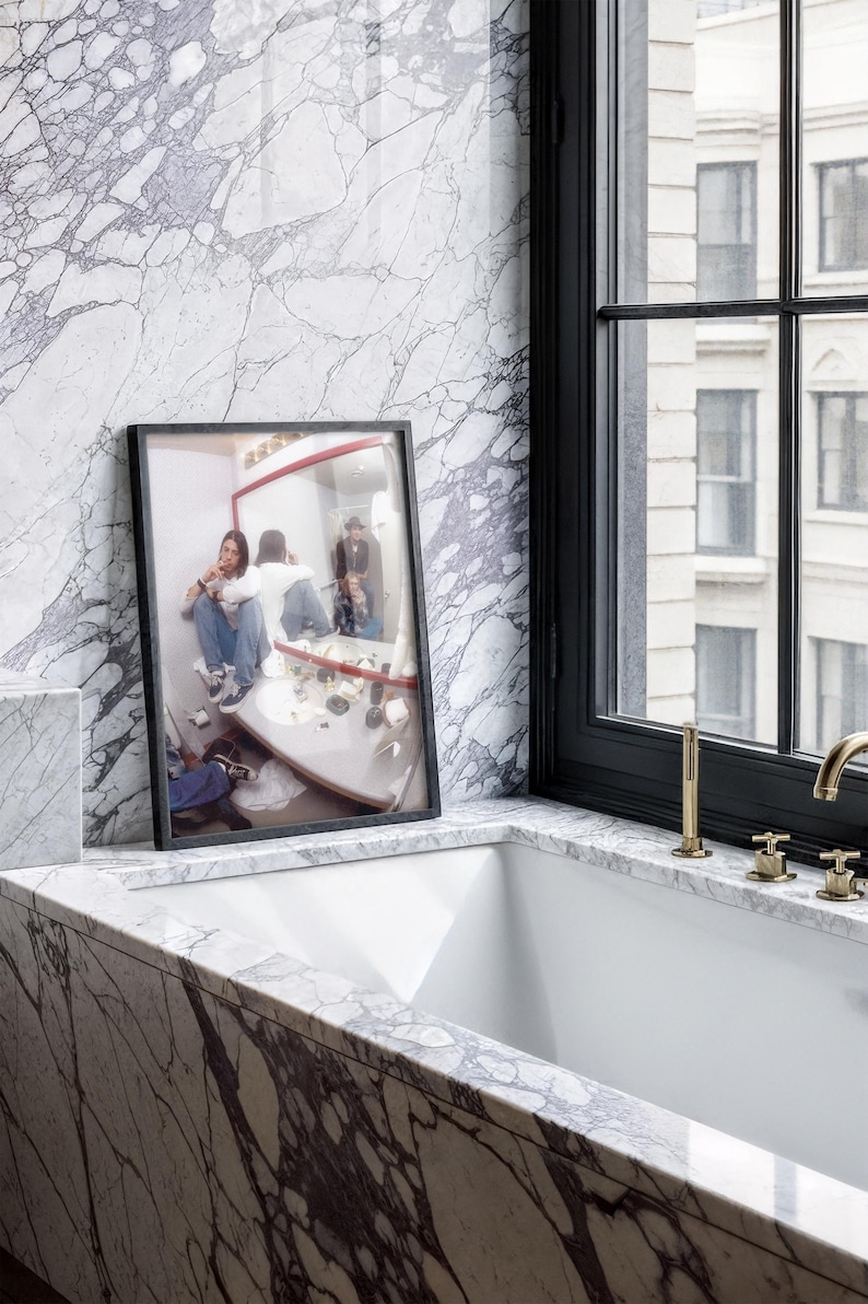 Pode incluir: Uma fotografia emoldurada de uma pessoa em uma casa de banho, repousando sobre uma bancada de m&aacute;rmore. A fotografia est&aacute; em uma moldura preta, e a casa de banho tem uma parede de m&aacute;rmore e uma janela com moldura preta. Ferragens douradas s&atilde;o vis&iacute;veis.