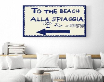 May include: A white sign with blue text and illustrations that reads "To the Beach Alla Spiaggia" with a blue arrow pointing left. The sign has a scalloped border.