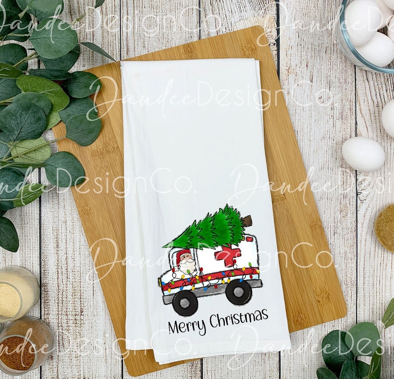 Pu&ograve; includere: Un asciugamano da cucina bianco con un'illustrazione di cartone animato di Babbo Natale che guida un'ambulanza con un albero di Natale in cima. L'ambulanza &egrave; decorata con luci di Natale. Il testo "Buon Natale" &egrave; stampato sotto l'immagine.