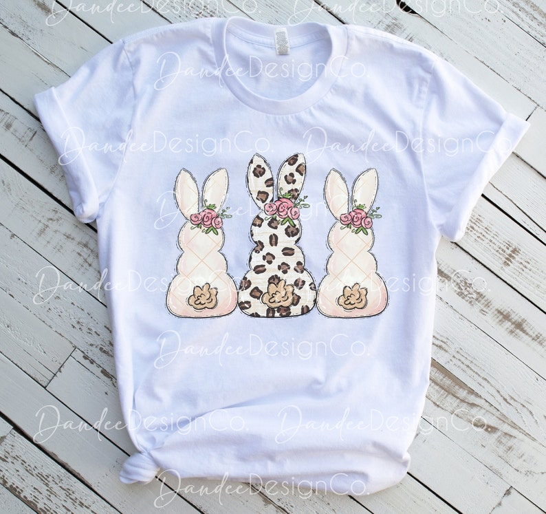 May include: Three Easter bunny-shaped figures, one with a leopard print pattern, and two with a white quilted pattern. Each bunny has a pink flower crown and a pink bow.
