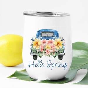 May include: White stainless steel tumbler with a blue pickup truck filled with pink and yellow flowers. The text "Hello Spring" is printed on the tumbler.