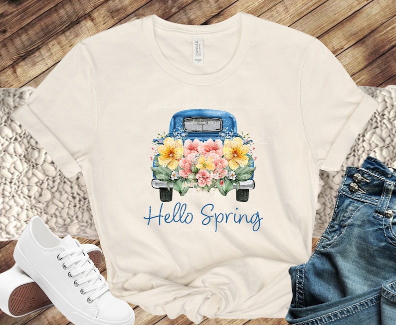 May include: A white t-shirt with a blue pickup truck carrying a bouquet of yellow and pink flowers. The text "Hello Spring" is printed below the truck.