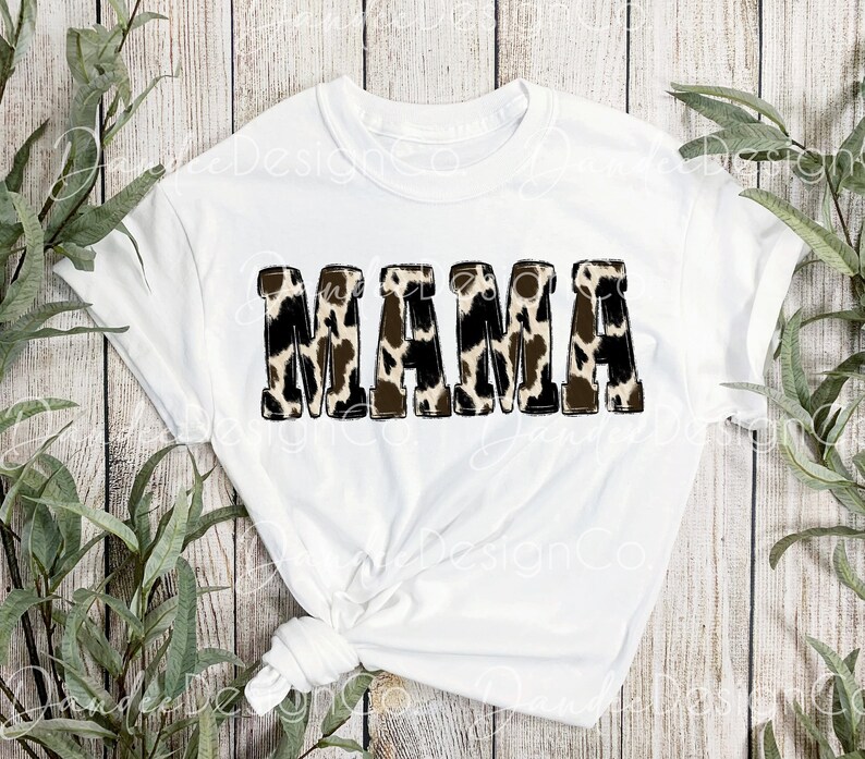 Puede incluir: Camiseta blanca con la palabra "MAMA" en letras negras delineadas con un estampado de leopardo marr&oacute;n y blanco.