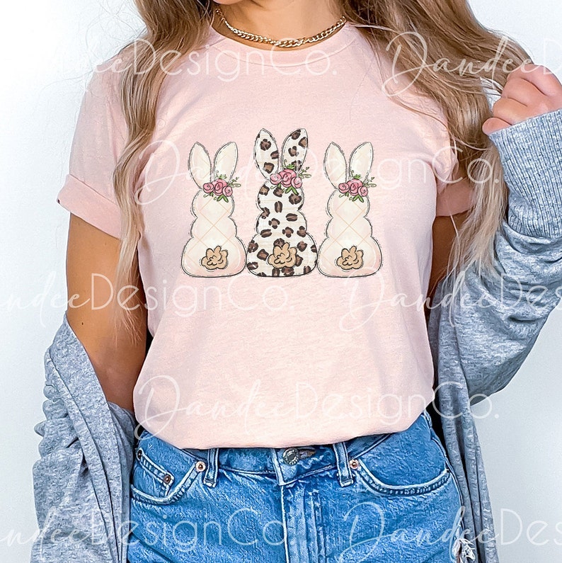 May include: A pink t-shirt with a graphic of three bunnies. The middle bunny is wearing a leopard print pattern and the other two bunnies are white with pink flowers.