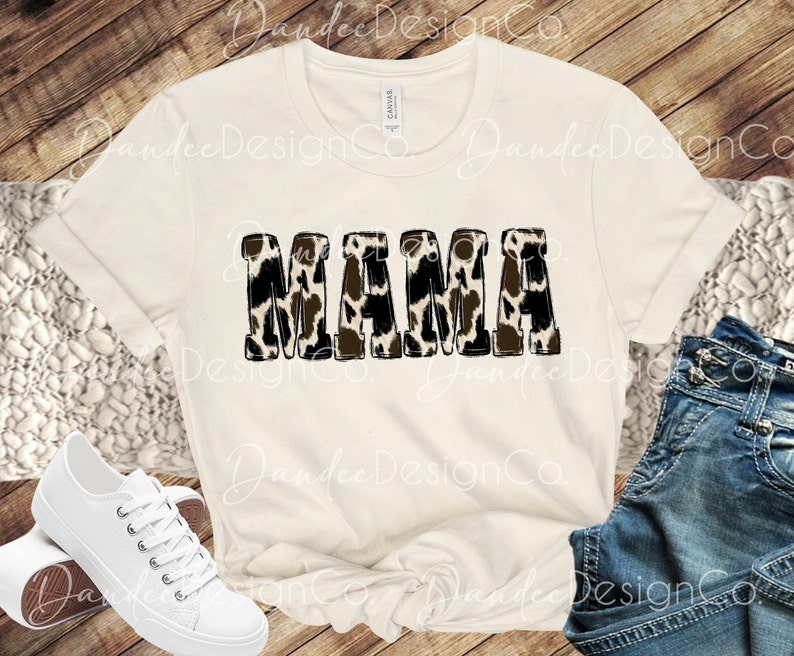 Puede incluir: Una camiseta blanca con la palabra "MAMA" impresa en letras negras con un estampado de leopardo marr&oacute;n y blanco.