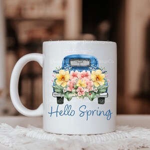 May include: White ceramic mug with a blue pickup truck filled with yellow and pink flowers. The text "Hello Spring" is printed on the mug.