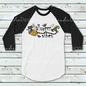 May include: A white and black baseball style t-shirt with a black and green Halloween themed graphic. The graphic features a cat riding a broomstick with a witch's hat and the text "Halloween vibes".