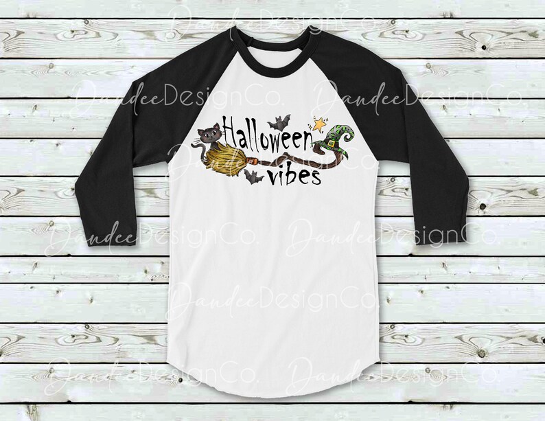 May include: A white and black baseball style t-shirt with a black and green Halloween themed graphic. The graphic features a cat riding a broomstick with a witch's hat and the text "Halloween vibes".