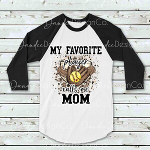 May include: White and black baseball raglan t-shirt with a brown and white graphic of a softball, glove, and baseball diamond. The graphic includes the text "My Favorite Player Calls Me Mom".