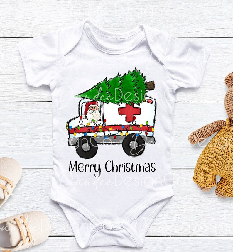 Pu&ograve; includere: Un body bianco per neonato con un'immagine di cartone animato di Babbo Natale che guida un'ambulanza con un albero di Natale in cima. L'ambulanza &egrave; decorata con luci di Natale. Il testo "Buon Natale" &egrave; stampato sotto l'immagine.