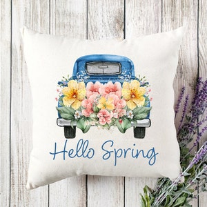 May include: A blue pickup truck with a bed full of yellow and pink flowers. The truck has the words "Hello Spring" written on the front.