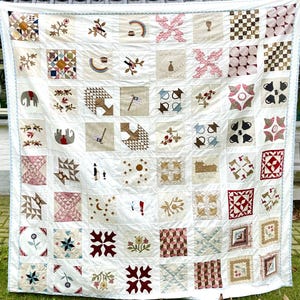 May include: A patchwork quilt featuring a range of colourful squares and patterns. The quilt is made from different fabrics, including red, blue, green, and white. The quilt is hanging on a white wall.