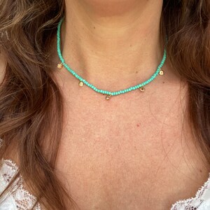 Pu&ograve; includere: Una collana di perline turchesi con piccoli ciondoli a forma di conchiglia dorata. La collana &egrave; indossata intorno al collo. Le perline sono piccole e ben distanziate, creando un look sottile ed elegante. Un gioiello delicato.