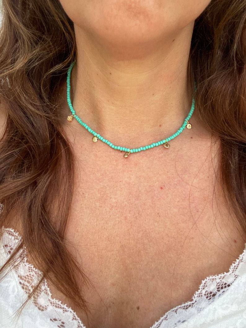 Pu&ograve; includere: Una collana di perline turchesi con piccoli ciondoli a forma di conchiglia dorata. La collana &egrave; indossata intorno al collo. Le perline sono piccole e ben distanziate, creando un look sottile ed elegante. Un gioiello delicato.