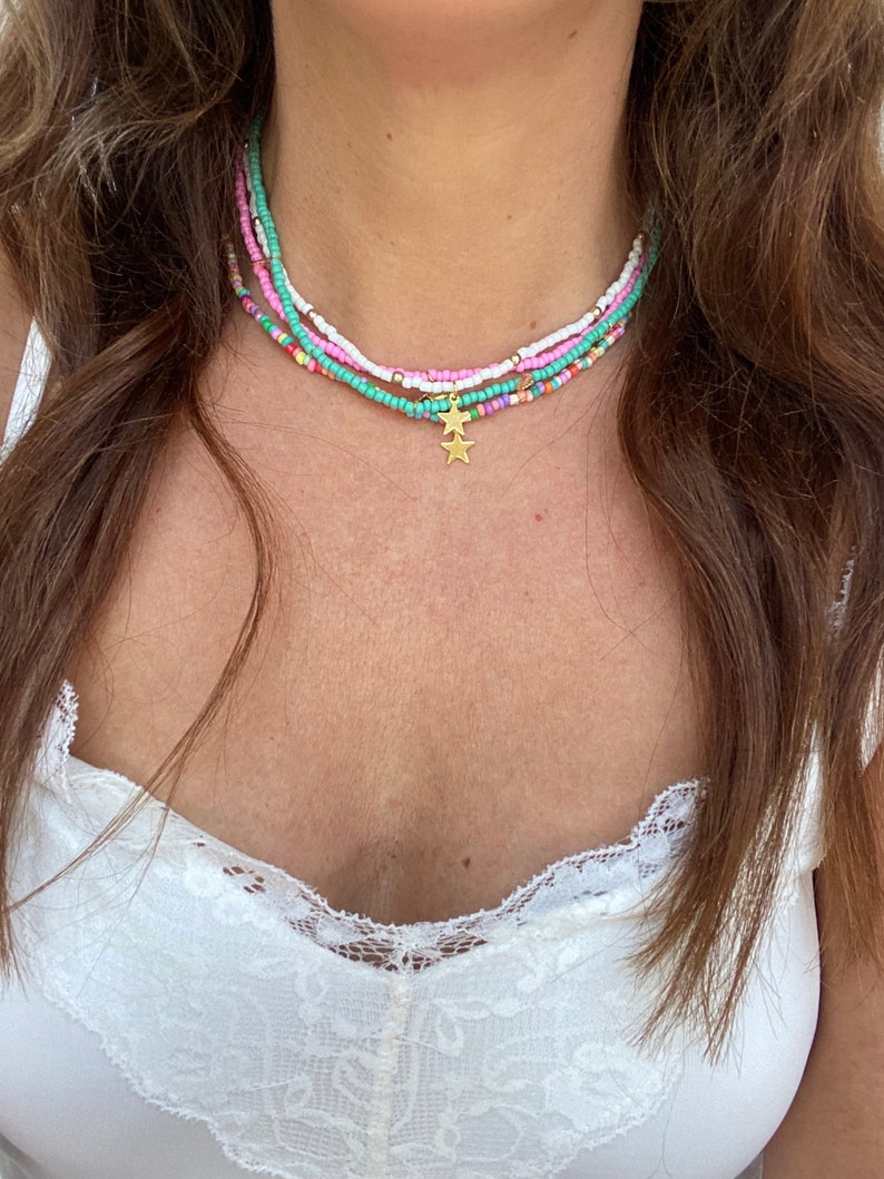 Pu&ograve; includere: Collana di perline a pi&ugrave; fili nei toni pastello, rosa, bianco e turchese. La collana ha un ciondolo a forma di stella dorata. La collana &egrave; indossata intorno al collo.