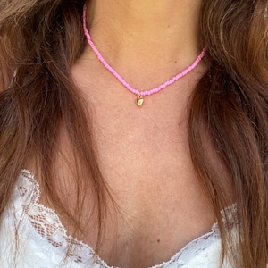 Pu&ograve; includere: Una delicata collana di perline rosa con un piccolo ciondolo a forma di cuore dorato. La collana &egrave; a girocollo, con minuscole perline rosa infilate insieme. Il ciondolo a forma di cuore dorato pende al centro, aggiungendo un tocco di eleganza.