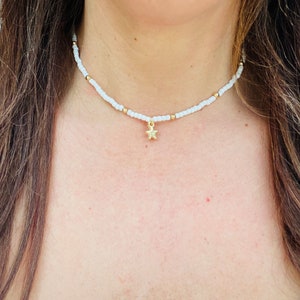 Pu&ograve; includere: Collana girocollo con perline bianche con dettagli dorati e un ciondolo a stella dorata. La collana &egrave; indossata intorno al collo. Le piccole perline distanziate creano un design semplice ed elegante. Un gioiello delicato.