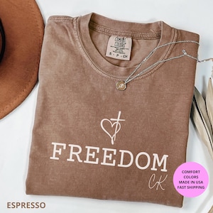 Freedom Christian shirt Comfort Colors®, tribute to Charlie K design honoring God, Family, and Country. Minimalist cross and heart artwork symbolizing faith and freedom. Made with 100% US cotton, garment-dyed for softness, relaxed unisex fit (S–4XL). Perfect for church, worship, rallies, or everyday wear. Available in Moss, Ivory, Pepper, Blue Jean, and Espresso. A meaningful religious gift, patriotic shirt, Christian apparel, faith tee, spiritual shirt, inspirational Christian merch.