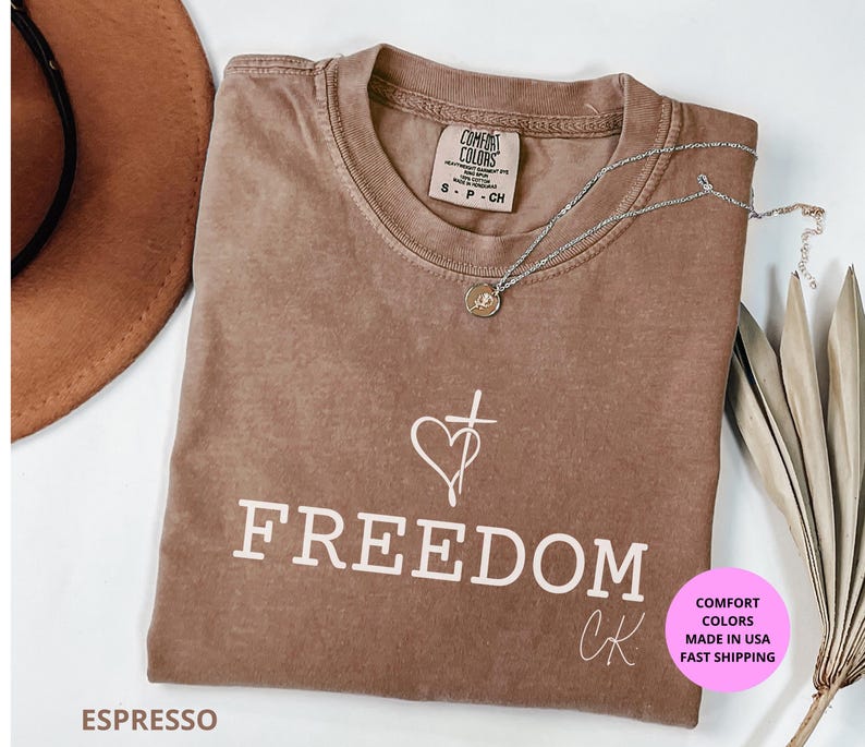 Freedom Christian shirt Comfort Colors®, tribute to Charlie K design honoring God, Family, and Country. Minimalist cross and heart artwork symbolizing faith and freedom. Made with 100% US cotton, garment-dyed for softness, relaxed unisex fit (S–4XL). Perfect for church, worship, rallies, or everyday wear. Available in Moss, Ivory, Pepper, Blue Jean, and Espresso. A meaningful religious gift, patriotic shirt, Christian apparel, faith tee, spiritual shirt, inspirational Christian merch.